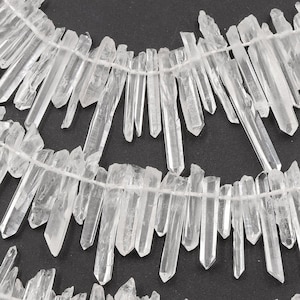 May include: Strands of clear quartz crystal points, strung together on a thin, white cord. The crystals vary in size and shape, with sharp, pointed ends. The background is a solid black.