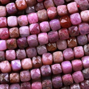 May include: A strand of pink ruby gemstone beads, each bead is faceted and has a square shape.