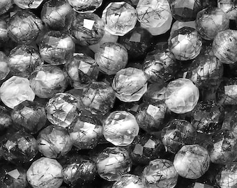 May include: A strand of faceted, clear quartz beads with black inclusions. The beads are round and have a smooth, polished finish.