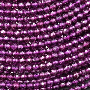 May include: Close-up of a collection of faceted, deep purple beads. The beads are strung together, creating a curved shape. The beads have a reflective, shiny surface, and are a rich, dark shade of purple.