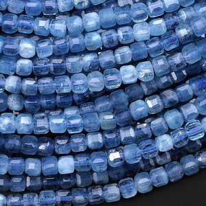 May include: A strand of light blue gemstone beads, each bead is faceted and has a square shape.