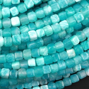 May include: A strand of turquoise blue gemstone beads, each bead is a square shape with slightly rounded edges.