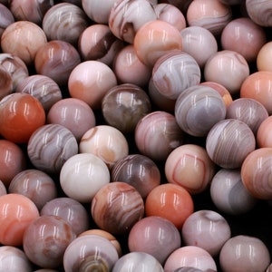 May include: A strand of pink and brown agate beads. The beads are round and have a smooth, polished finish. The agate is a natural stone with a unique pattern of stripes and swirls.