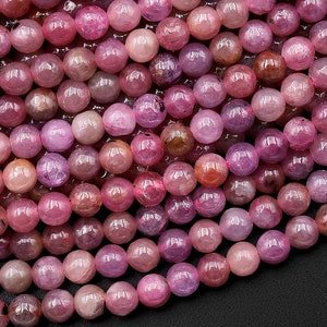 May include: A strand of pink ruby gemstone beads. The beads are round and have a smooth, polished finish. The beads are strung on a clear thread.