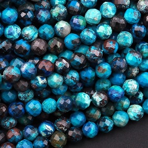May include: A close-up of a strand of blue and black gemstone beads. The beads are faceted and have a rough, natural texture.