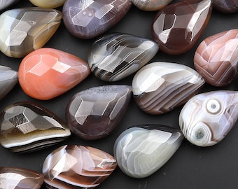 May include: A collection of agate gemstone beads in various shades of brown, grey, and white. The beads are faceted and have a teardrop shape.