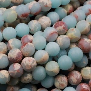 K&ouml;nnte beinhalten: Eine Str&auml;hne aus blauen, wei&szlig;en und roten Jaspisperlen. Die Perlen sind rund und haben eine matte Oberfl&auml;che.