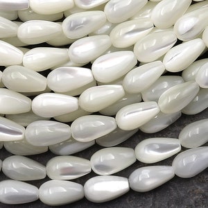 May include: A strand of white pearlescent teardrop-shaped beads. The beads are smooth and have a subtle iridescent sheen.