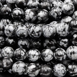 May include: A strand of black and white snowflake obsidian beads. The beads are round and have a speckled pattern.