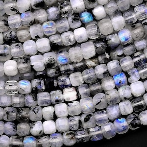 May include: A strand of white and black gemstone beads with iridescent blue and green flashes. The beads are square shaped and have a smooth, polished finish.