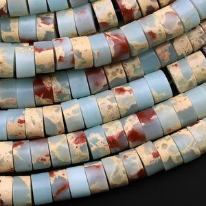 May include: A close-up of a strand of light blue and red jasper beads. The beads are round and have a speckled pattern.