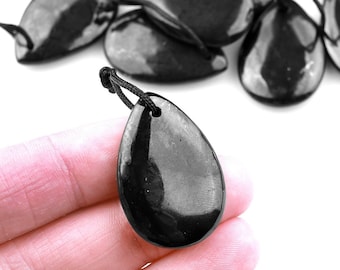 Op de afbeelding: Een stapel zwarte obsidiaan druppel hangers met een zwarte koord bevestigd. Een hanger wordt in een hand gehouden.