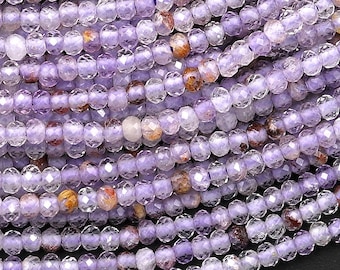 May include: Close-up of a collection of small, faceted beads in shades of lavender and clear. The beads are strung together, creating a flowing, textured surface. Some beads have hints of orange and brown.