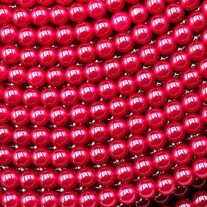 Może przedstawiać: Szereg jasnoczerwonych, okrągłych koralików. Korale są gładkie i błyszczące.