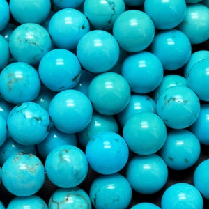 May include: A close-up of a pile of turquoise blue round beads. The beads are smooth and have a slight sheen.
