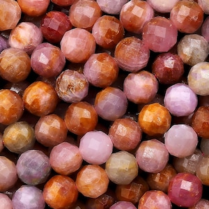 May include: A strand of faceted gemstone beads in shades of pink, orange, and brown. The beads are all approximately the same size and have a smooth, polished finish.