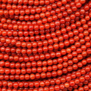 Puede incluir: Una hebra de cuentas de coral de color naranja brillante. Las cuentas son redondas y lisas, y están dispuestas en un patrón de primer plano.