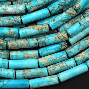 May include: A strand of turquoise blue gemstone beads with brown and white marbling. The beads are cylindrical and have a smooth, polished finish.
