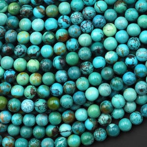 May include: A close-up shot of a collection of turquoise beads. The beads are round and vary in shades of blue and green, with some showing brown and white marbling. The beads are tightly packed together, filling the frame.