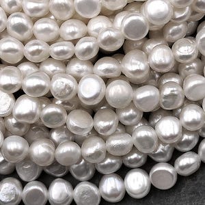 Peut inclure: Gros plan sur un tas de perles blanches d'eau douce. Les perles sont de forme irrégulière, avec une surface lisse et réfléchissante. Les perles sont enfilées, suggérant qu'elles sont destinées à la création de bijoux.