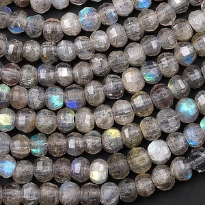 May include: Close-up of strands of faceted labradorite beads. The beads are a mix of gray and translucent with flashes of blue, green, and yellow iridescence. The beads are strung together, creating a textured surface.