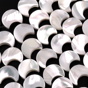 May include: A collection of white mother of pearl shell beads in the shape of half moons. The beads are arranged in rows, overlapping each other.