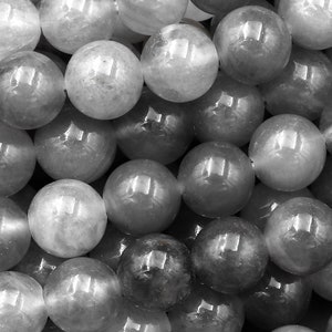 May include: A close-up of a pile of round, gray and white gemstone beads. The beads are smooth and shiny, and they have a slight translucence.