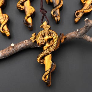 Puede incluir: Una colección de colgantes tallados en ojo de tigre con diseño de dragón. Los colgantes, de color marrón dorado, están suspendidos de cordones marrones. Los grabados de dragones son detallados e intrincados, con un acabado pulido.