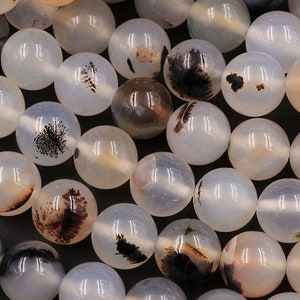 Puede incluir: Una hebra de cuentas de ágata blanca con inclusiones dendríticas negras y marrones. Las cuentas son redondas y lisas, y tienen un acabado natural y pulido.