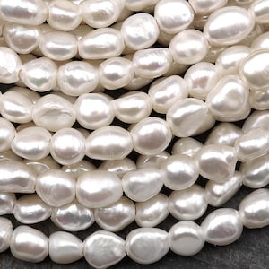 Puede incluir: Primer plano de una colecci&oacute;n de perlas de agua dulce blancas cremosas de forma irregular. Las perlas est&aacute;n ensartadas, creando una superficie texturizada y luminosa. Las perlas tienen un aspecto natural y org&aacute;nico.