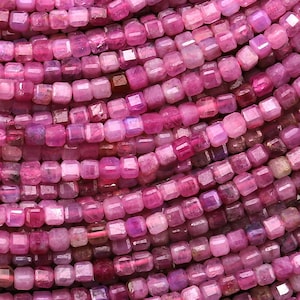 May include: A strand of pink ruby gemstone beads, each bead is faceted and has a square shape.
