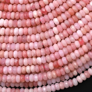 Puede incluir: Una hebra de cuentas de ópalo rosa, cada cuenta está facetada y tiene una forma ligeramente irregular. Las cuentas están enhebradas para crear una larga hebra de joyería.