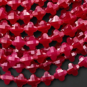 May include: Close-up of a collection of faceted, cross-shaped beads in a vibrant red hue. The beads are strung together, creating a textured and visually appealing surface. Ideal for jewelry making and crafting.
