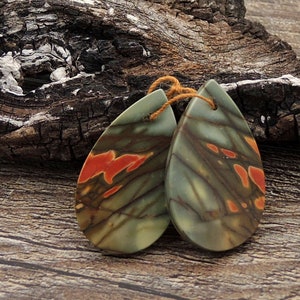 May include: A pair of teardrop-shaped earrings made from green, brown, and orange stone with a marbled pattern. The earrings are hanging from a piece of brown string.