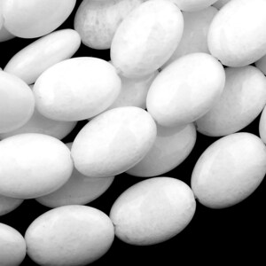 May include: A close-up of a pile of white oval-shaped beads. The beads are smooth and have a slightly textured surface.