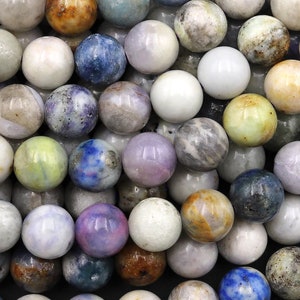 May include: A collection of round gemstone beads in various colors, including white, gray, blue, purple, and brown. The beads have a polished, smooth surface and are arranged closely together, creating a textured appearance. Ideal for jewelry making.