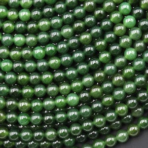 Puede incluir: Primer plano de una colección de cuentas de piedras preciosas verdes. Las cuentas son redondas y tienen un acabado brillante, con diferentes tonos de verde. Las cuentas están dispuestas muy juntas, llenando el marco.