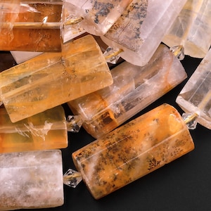 May include: A close-up of a pile of faceted, translucent, orange and white gemstone beads. The beads are rectangular in shape and have a natural, rough texture.