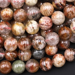 May include: A close-up of a pile of round, translucent, brown, white, and gray gemstone beads. The beads have a natural, rough texture and are perfect for jewelry making.