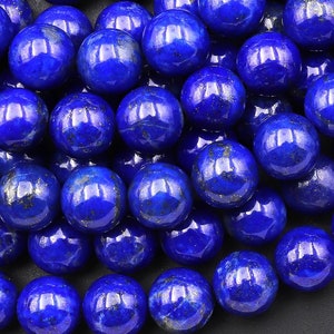 May include: A close-up of a pile of round, blue lapis lazuli beads. The beads are smooth and polished, with a slight shimmer.