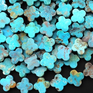 May include: A large pile of turquoise blue clover-shaped beads. The beads have a mottled, natural stone appearance.