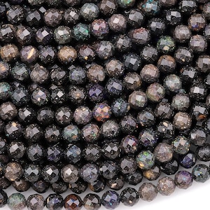 Może przedstawiać: Sznur fasetowanych koralików z czarnego opalu. Koraliki mają średnicę około 6 mm i ciemny, tęczowy połysk.