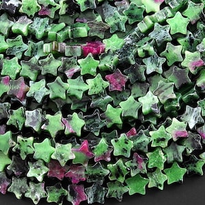 Könnte beinhalten: Eine Sammlung sternförmiger Perlen in Grün-, Schwarz- und Rosatönen. Die Perlen bestehen aus Steinmaterial und sind aufgefädelt. Die Sterne haben ein strukturiertes Aussehen und variieren in der Farbintensität.