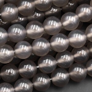 May include: A strand of round, grey agate beads. The beads are smooth and have a slight sheen.