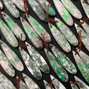 May include: A collection of green and white teardrop-shaped gemstone pendants with brown leather cords. The stones have a marbled pattern and are arranged in rows.
