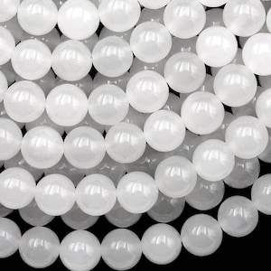 May include: A close-up shot of numerous white, round beads. The beads are smooth and shiny, with a pearlescent quality. They are tightly packed together, filling the frame. The beads appear to be made of a solid material, possibly stone or glass, and are uniform in size.