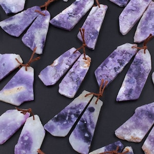 May include: A collection of 18 pairs of purple and white opal gemstone earrings. Each pair is tied together with a brown string.