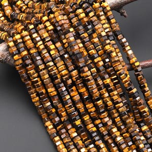 May include: Strands of faceted tiger eye gemstone beads in shades of brown and gold. The beads are strung together, creating a textured and natural appearance. The beads are displayed on a dark background.