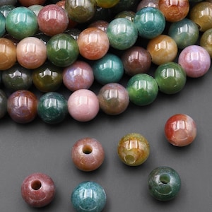 May include: A collection of gemstone beads in various colors, including green, brown, pink, and orange. The beads are round with a polished finish and a hole drilled through the center. The beads are suitable for jewelry making.