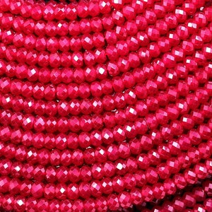 Può includere: Una collana di perline di pietra preziosa sfaccettata rosso vivo. Le perline sono rotonde e hanno una finitura liscia e lucida.